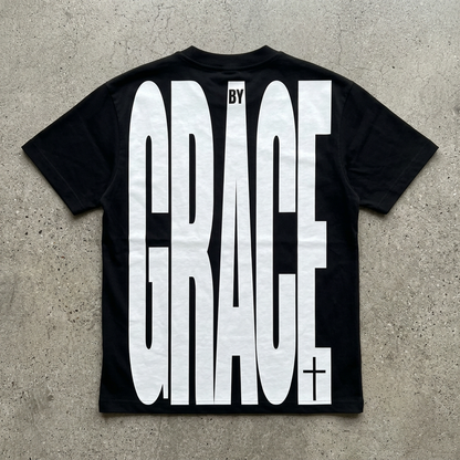 Black t-shirt with 'BY GRACE' text on a concrete surface