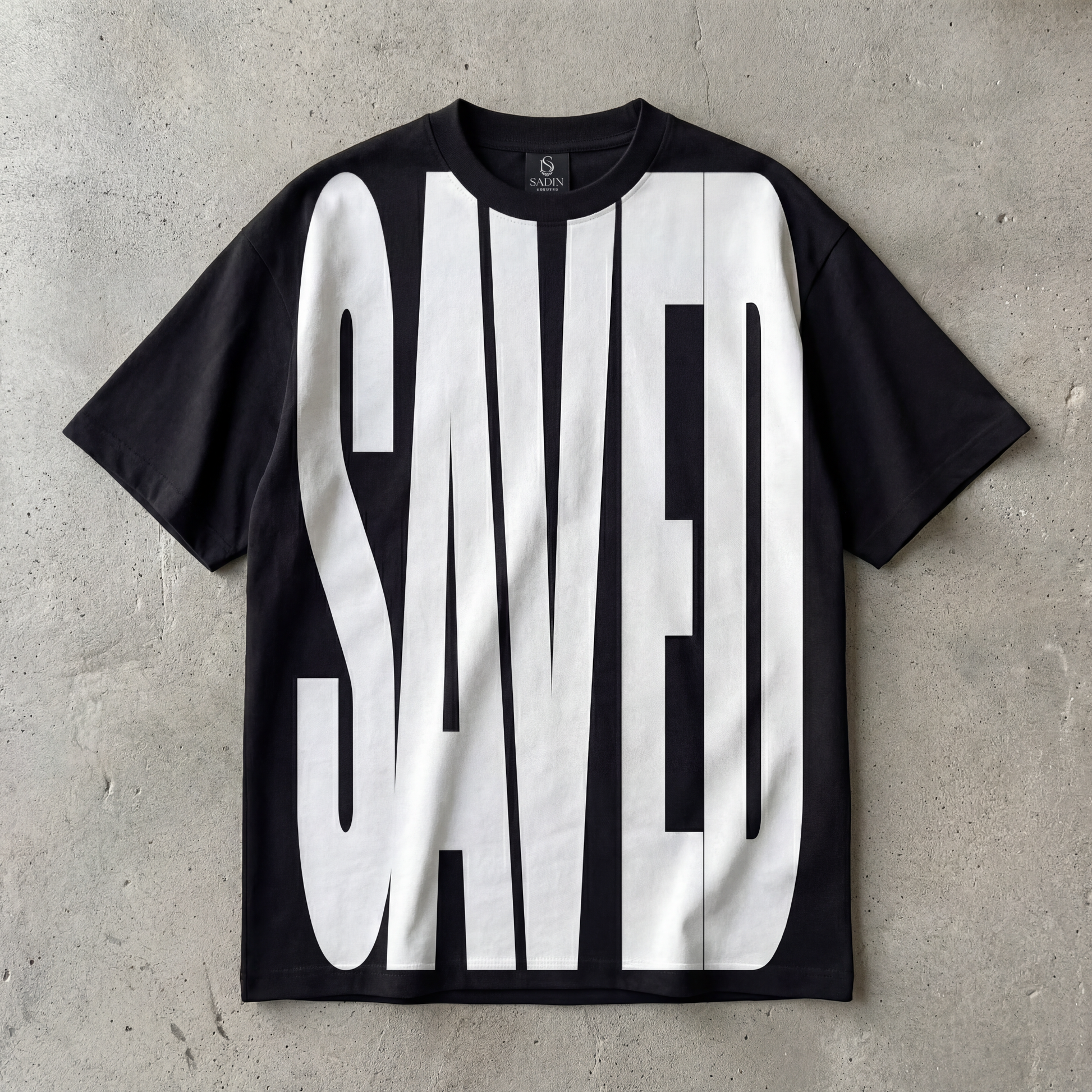 Black t-shirt with 'SAVED' printed in white on a concrete surface